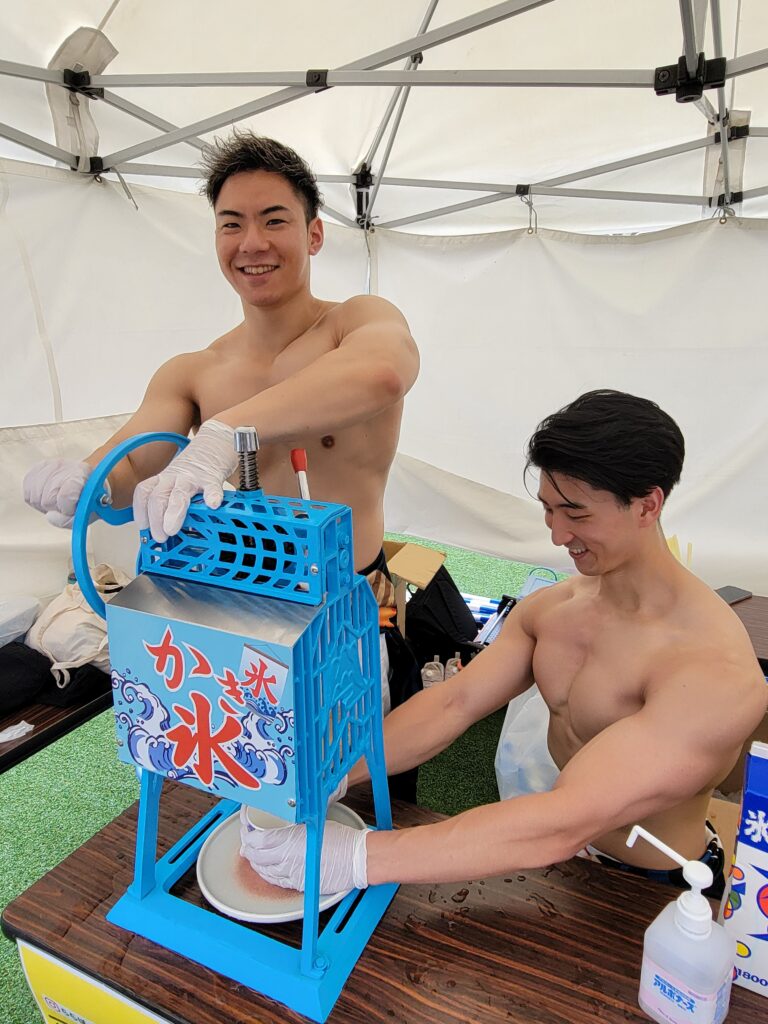 テントの中でメンバー2人が手動のかき氷機を使って氷を削っている様子