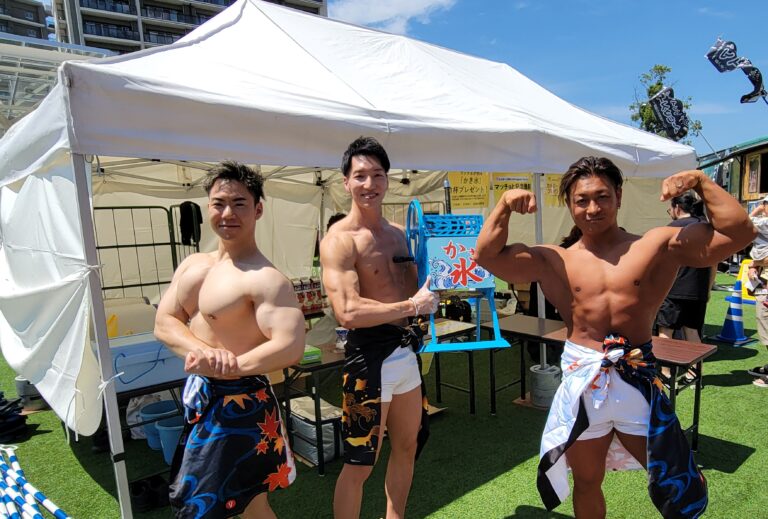 屋外のかき氷ブースの前で3人のメンバーがポーズをとる様子